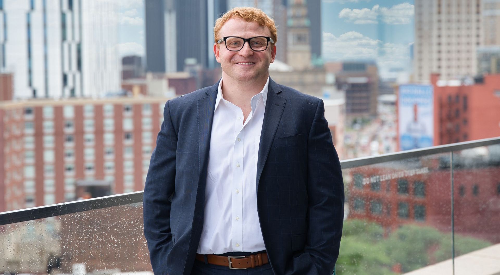 A man in a suit is smiling with his arms crossed.