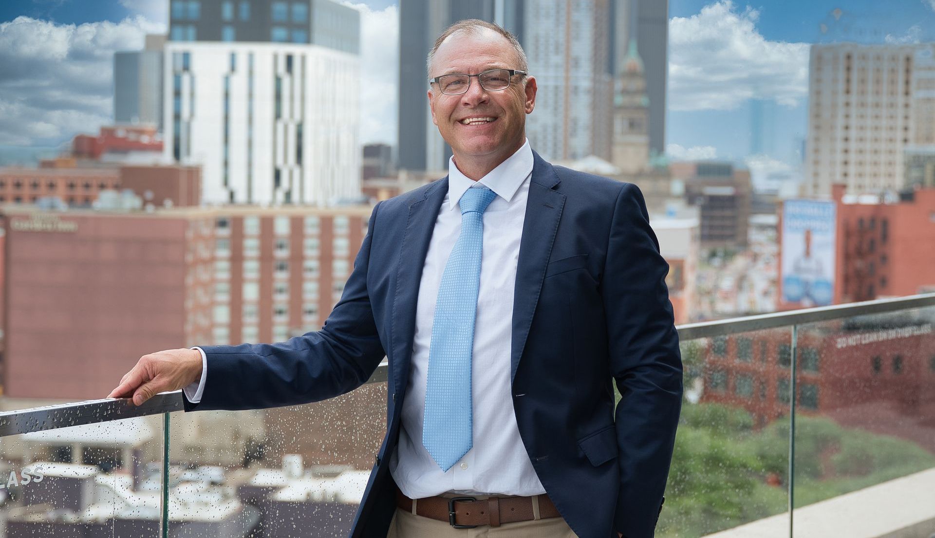 A man in a suit is smiling with his arms crossed.