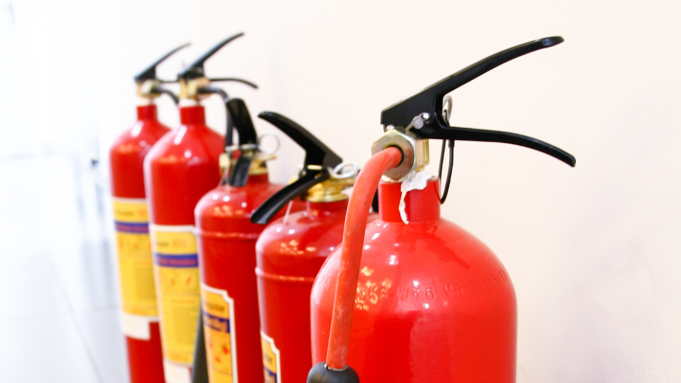 Red fire extinguishers lined up against a white wall.