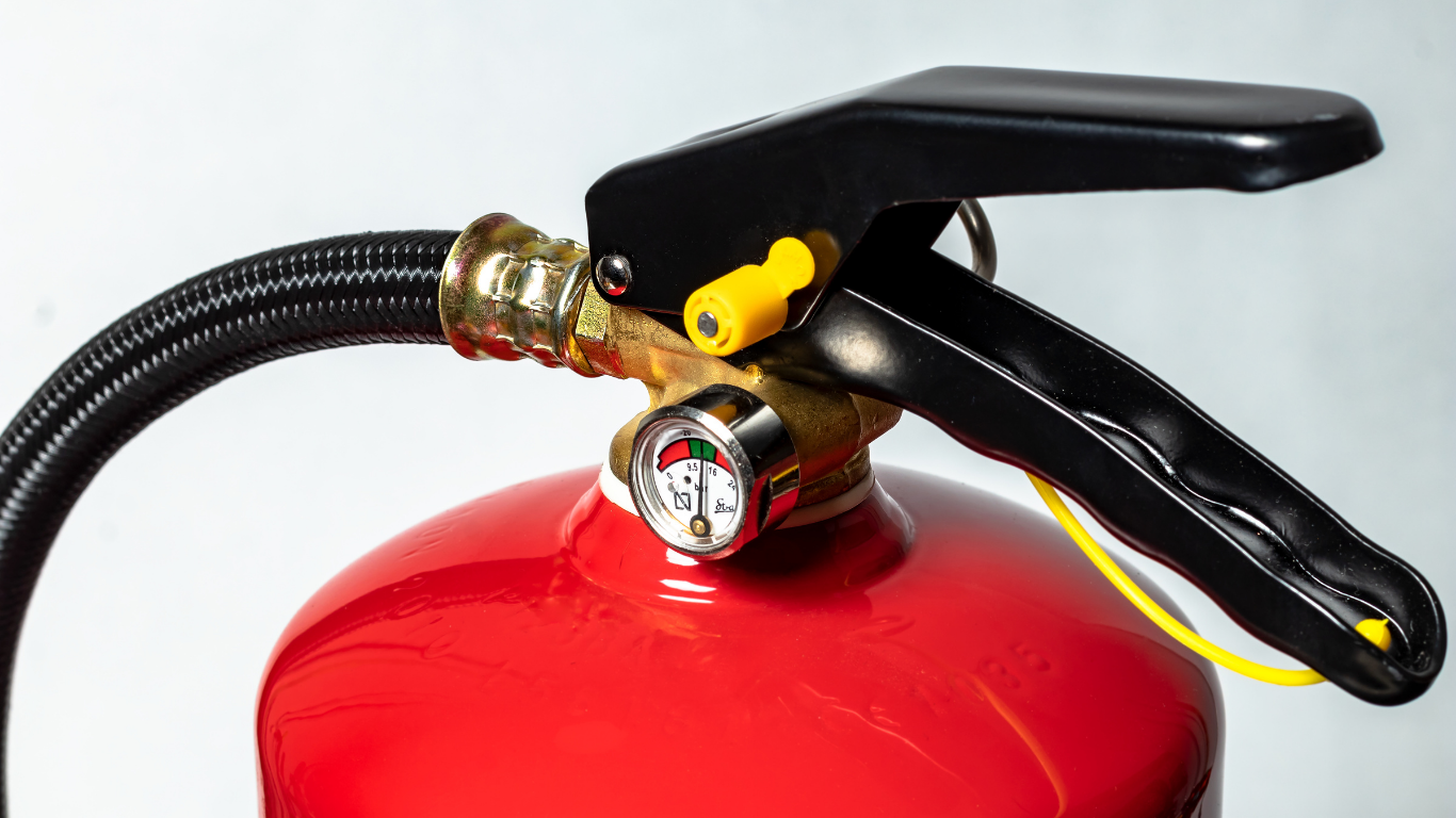 Red fire extinguisher with a black handle, gauge, and hose; ready to use.