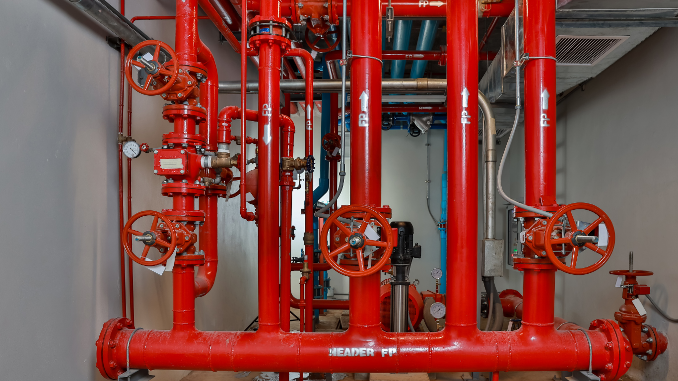 Red fire sprinkler system pipes and valves in a mechanical room.