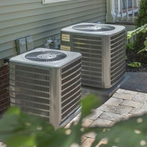 Two air conditioners are sitting on the side of a house.