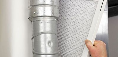 A person is holding a filter in front of a metal pipe.