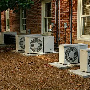 A row of air conditioners are sitting outside of a brick building.