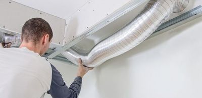 A man is installing a ventilation pipe from the ceiling.