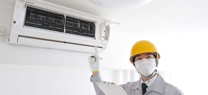 A man wearing a mask and hard hat is working on an air conditioner.