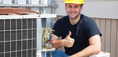 A man wearing a hard hat is giving a thumbs up while working on an air conditioner.