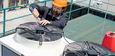 A man wearing a hard hat is working on a fan.