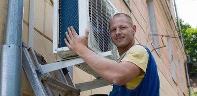 A man is installing an air conditioner on the side of a building.