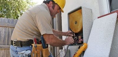 A man wearing a hard hat is working on a machine outside of a building.