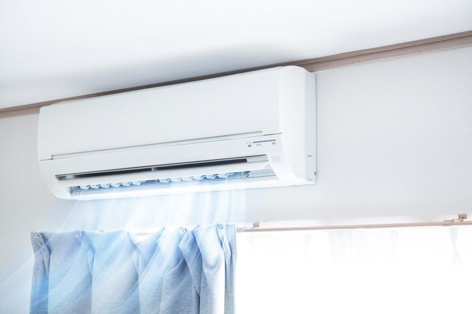 A white air conditioner is hanging from the ceiling in a room next to a window.