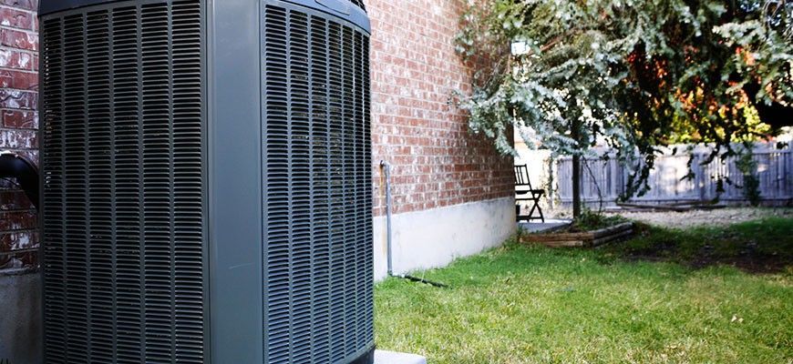 A large air conditioner is sitting in the backyard of a house.