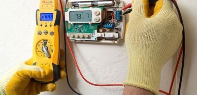 A person is working on a thermostat with a multimeter.