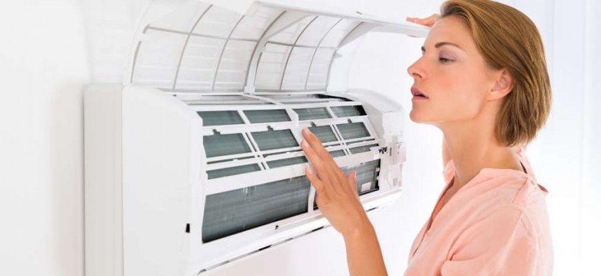 A woman is cleaning the filter of an air conditioner.