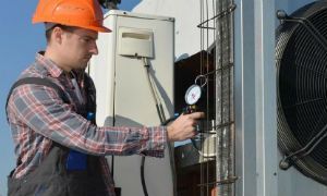 A man wearing a hard hat is working on an air conditioner.