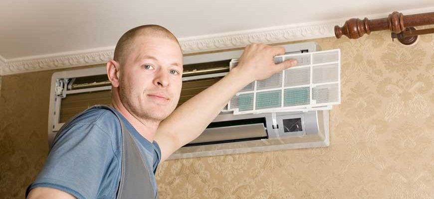 A man is cleaning an air conditioner with a filter.