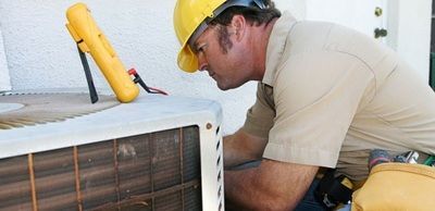 A man wearing a hard hat is working on an air conditioner.