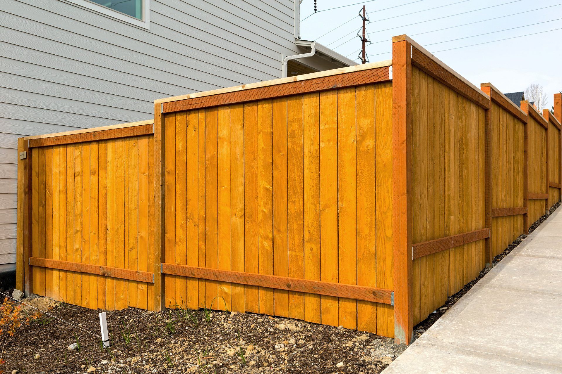 A recently stained wood privacy fence with top rail and cap