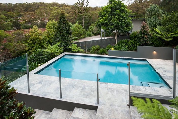 An aluminum and glass pool fence securing a concrete patio and pool on a hill in Cincinnati