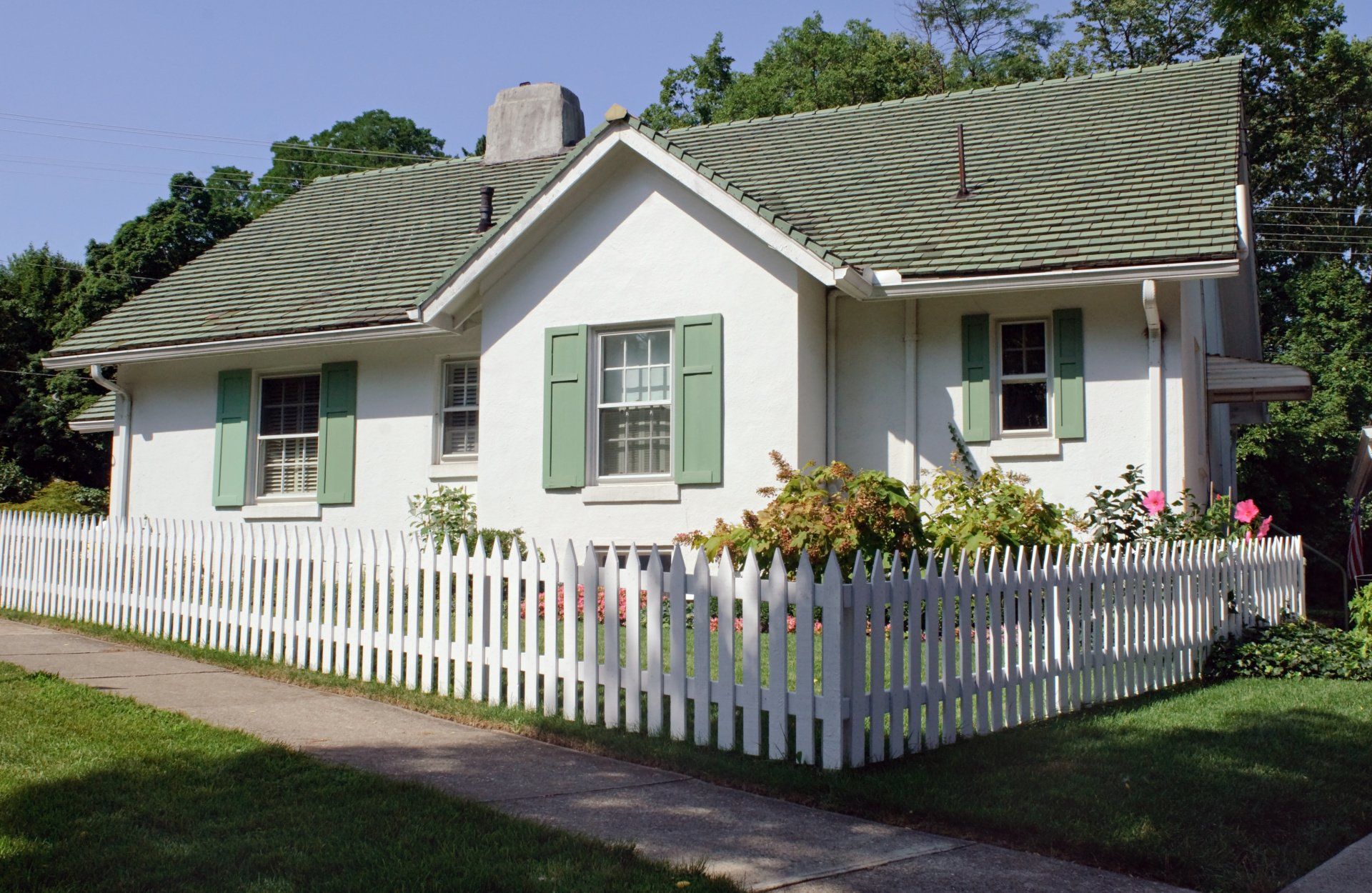 A white picket fence in the front yard of a white cottage