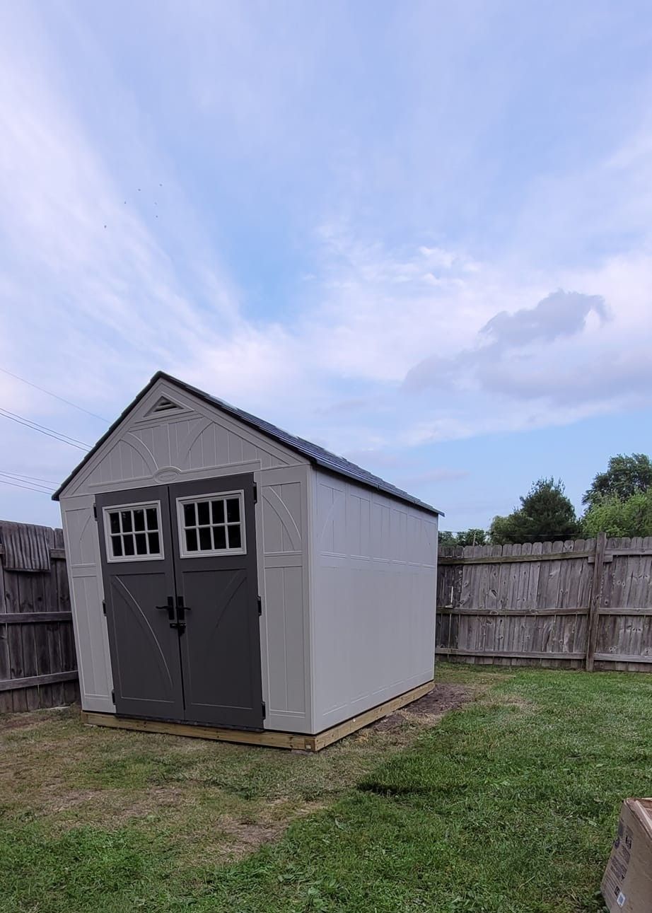 Gray shed with dark gray doors and roof against a cloudy sky, set in a grassy yard.