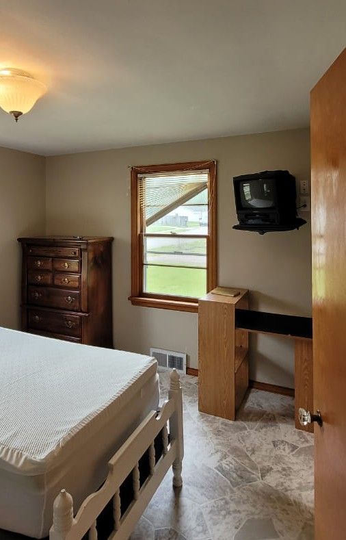 Bedroom with bed, dresser, desk, window, and mounted TV.