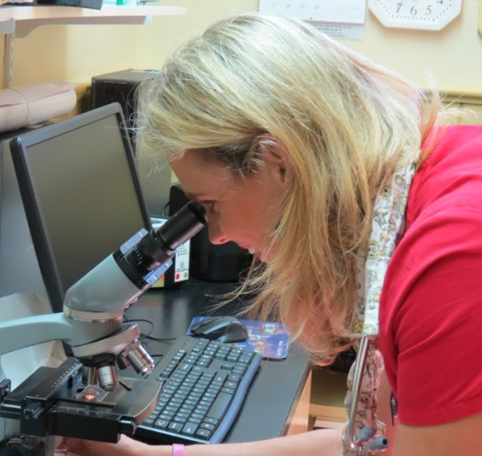 a woman in a red shirt is looking through a microscope