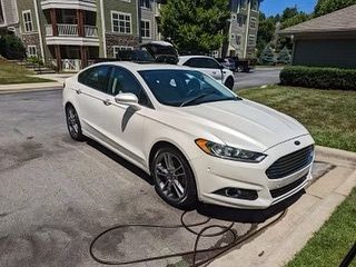 A white ford fusion is parked in a parking lot next to a house.