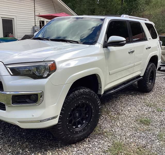 A white suv is parked on gravel in front of a house.