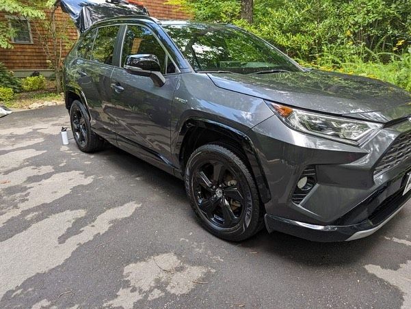 A toyota rav4 is parked in a driveway with its trunk open.