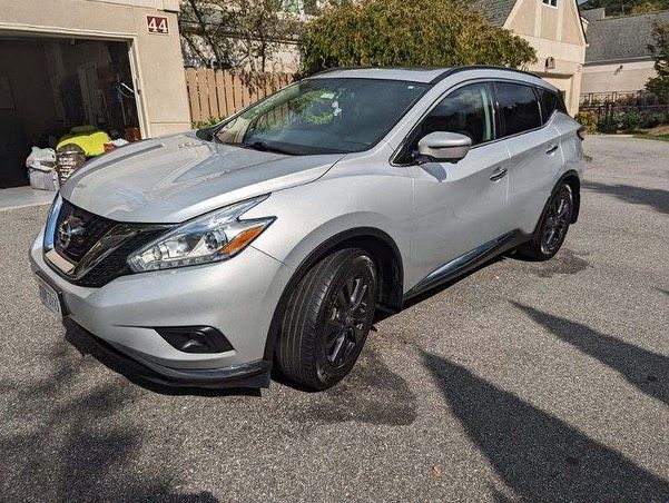 A silver nissan murano is parked in front of a garage.
