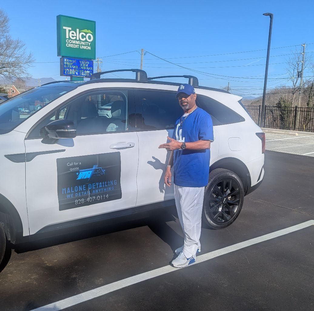 A man in a blue shirt is standing in front of a white car with a telco sign on it