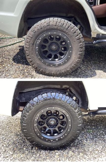 A white truck with black wheels and tires is parked on a gravel road.
