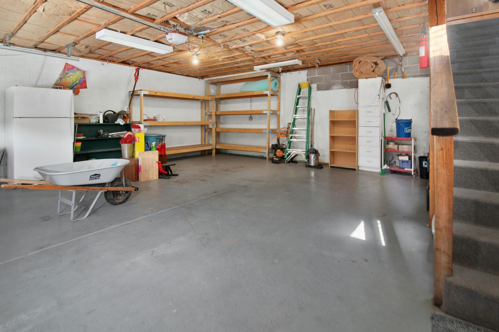 An empty garage with a wheelbarrow and a ladder