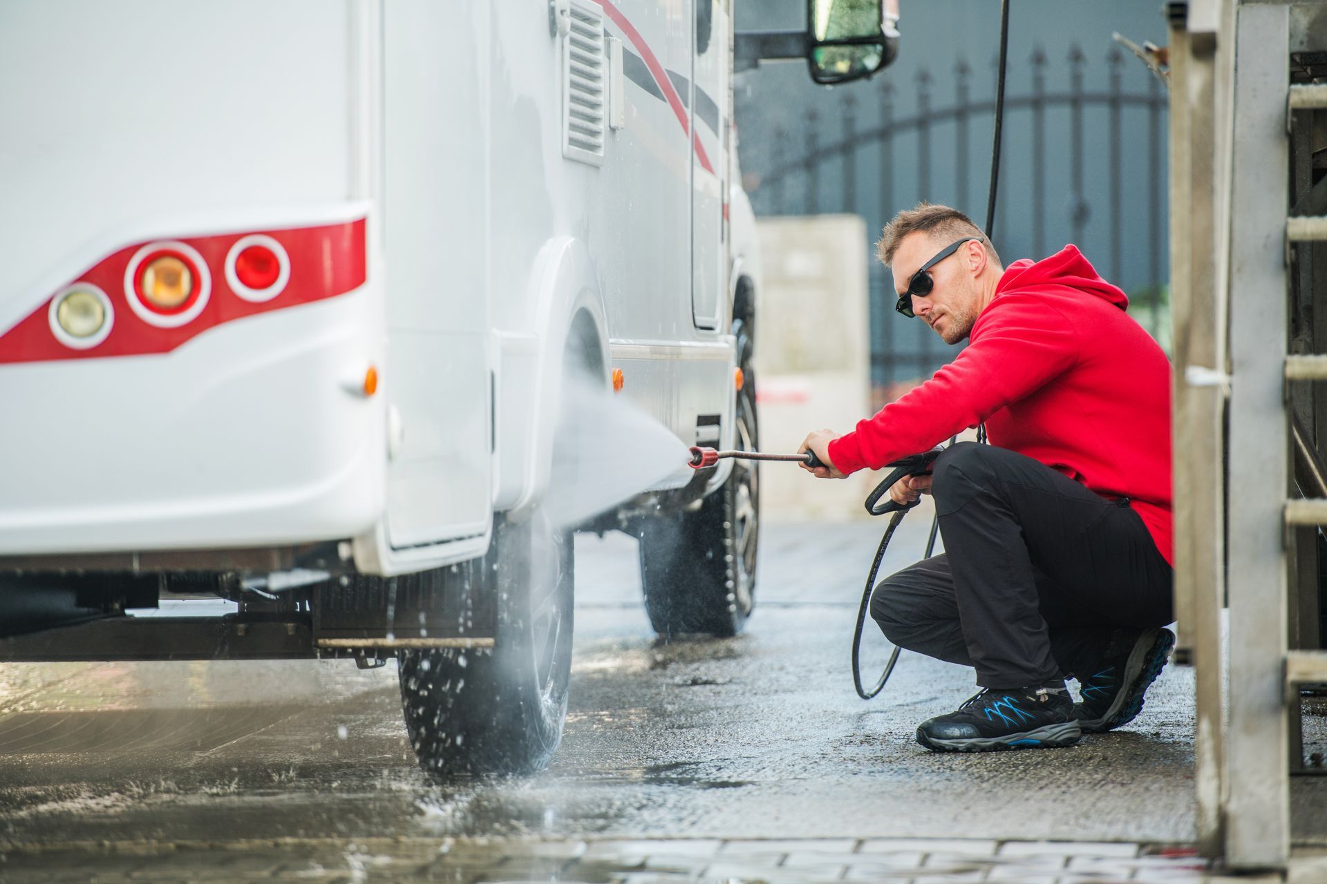 A man is kneeling down to wash a camper with a high pressure washer.