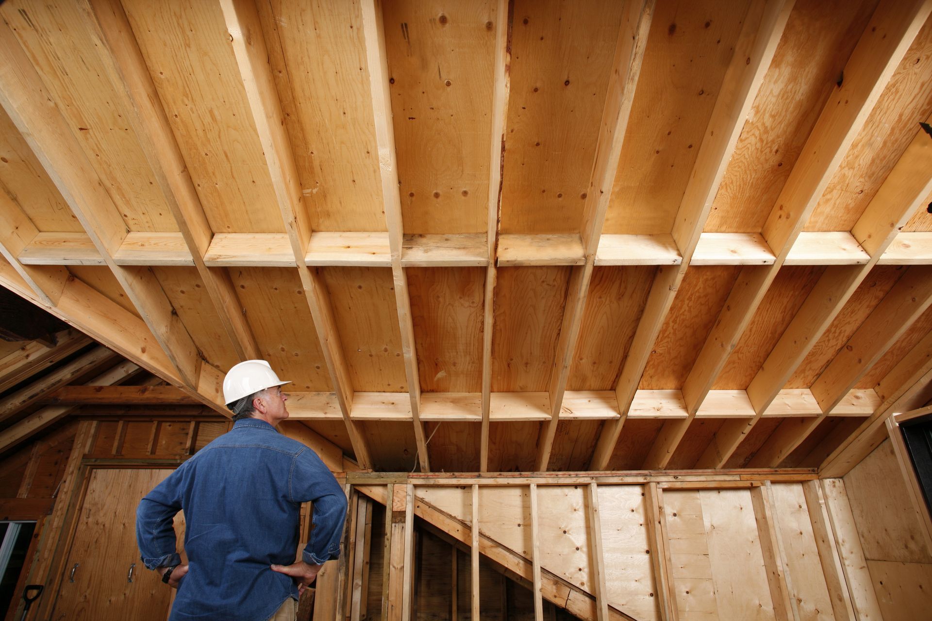 A man in a hard hat is looking up at the ceiling of a house under construction.