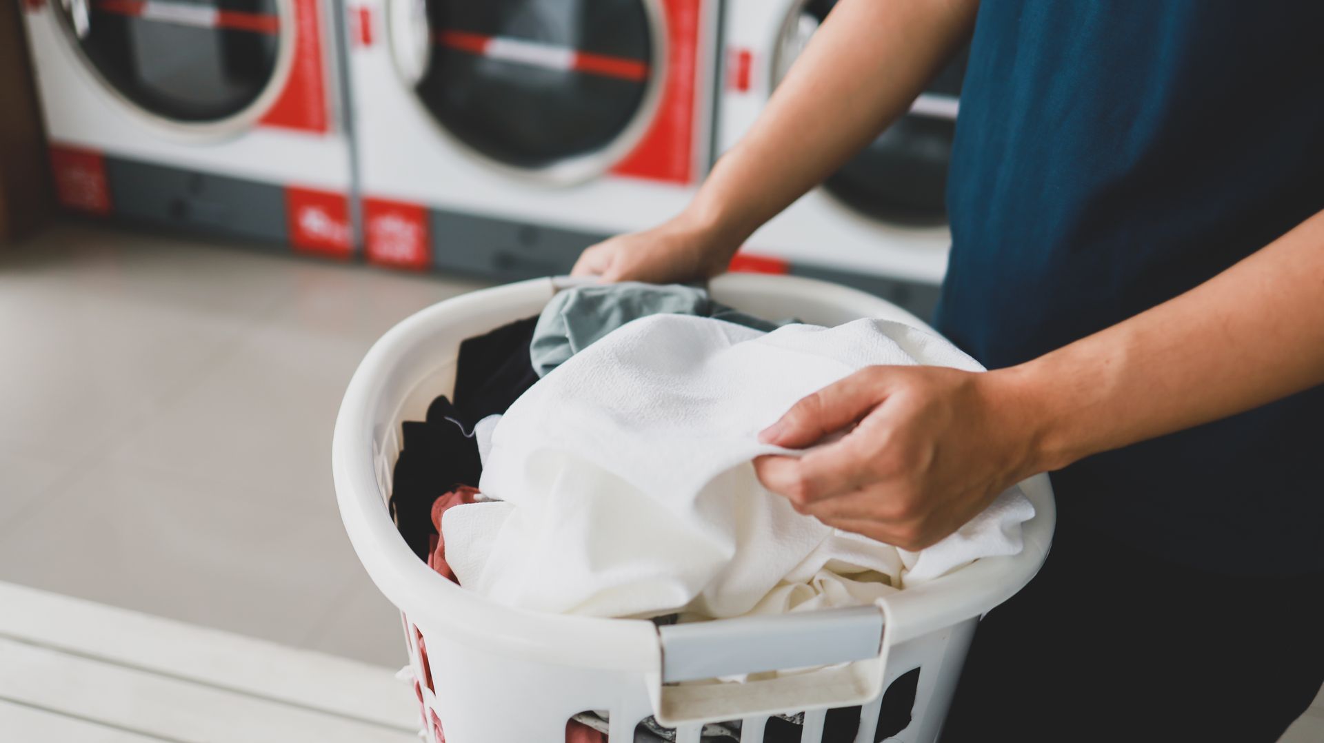 A person is holding a laundry basket full of clothes in a laundromat.