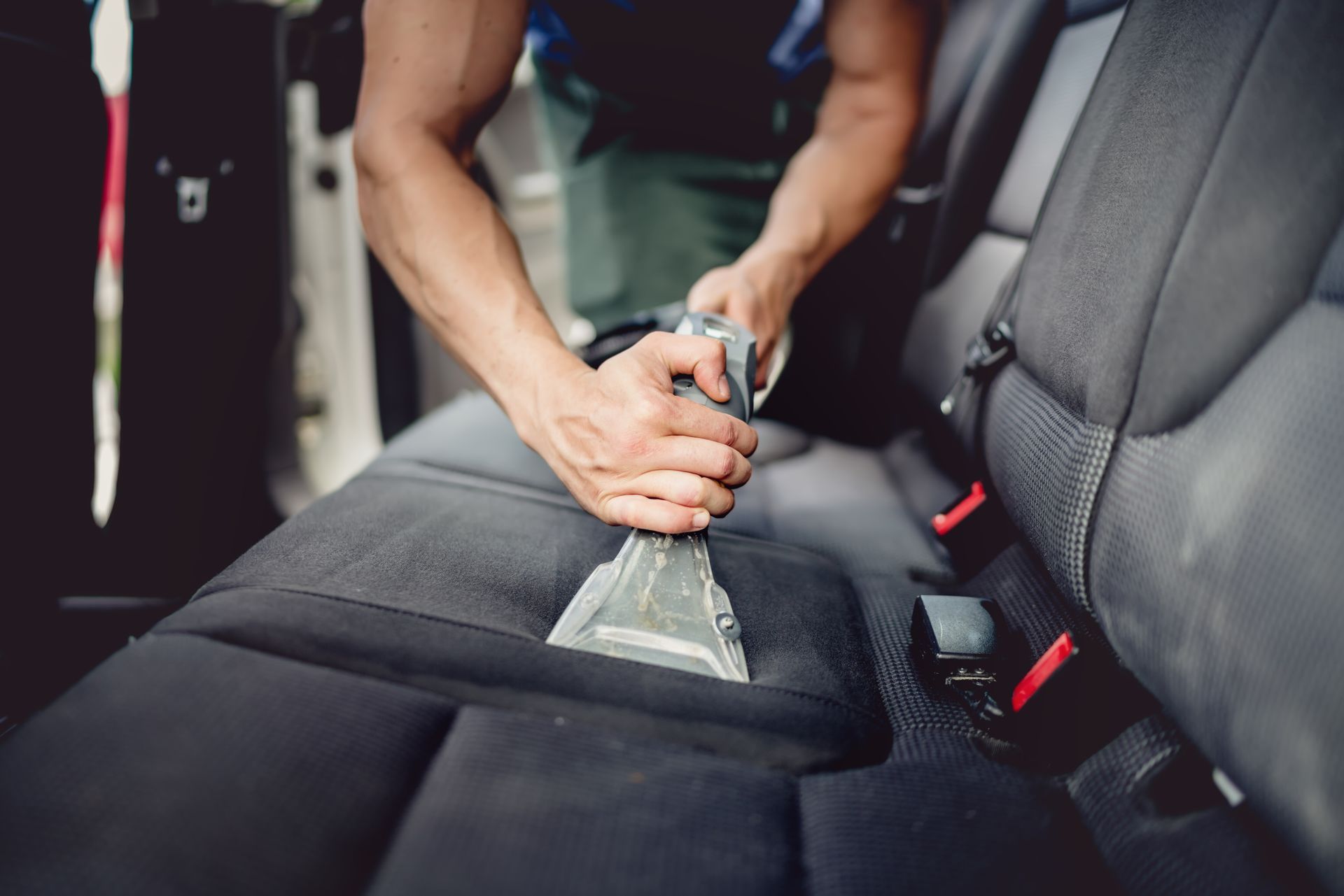 A man is cleaning the back seat of a car with a vacuum cleaner.