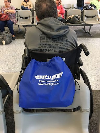 A man in a wheelchair with a blue bag attached to his back.