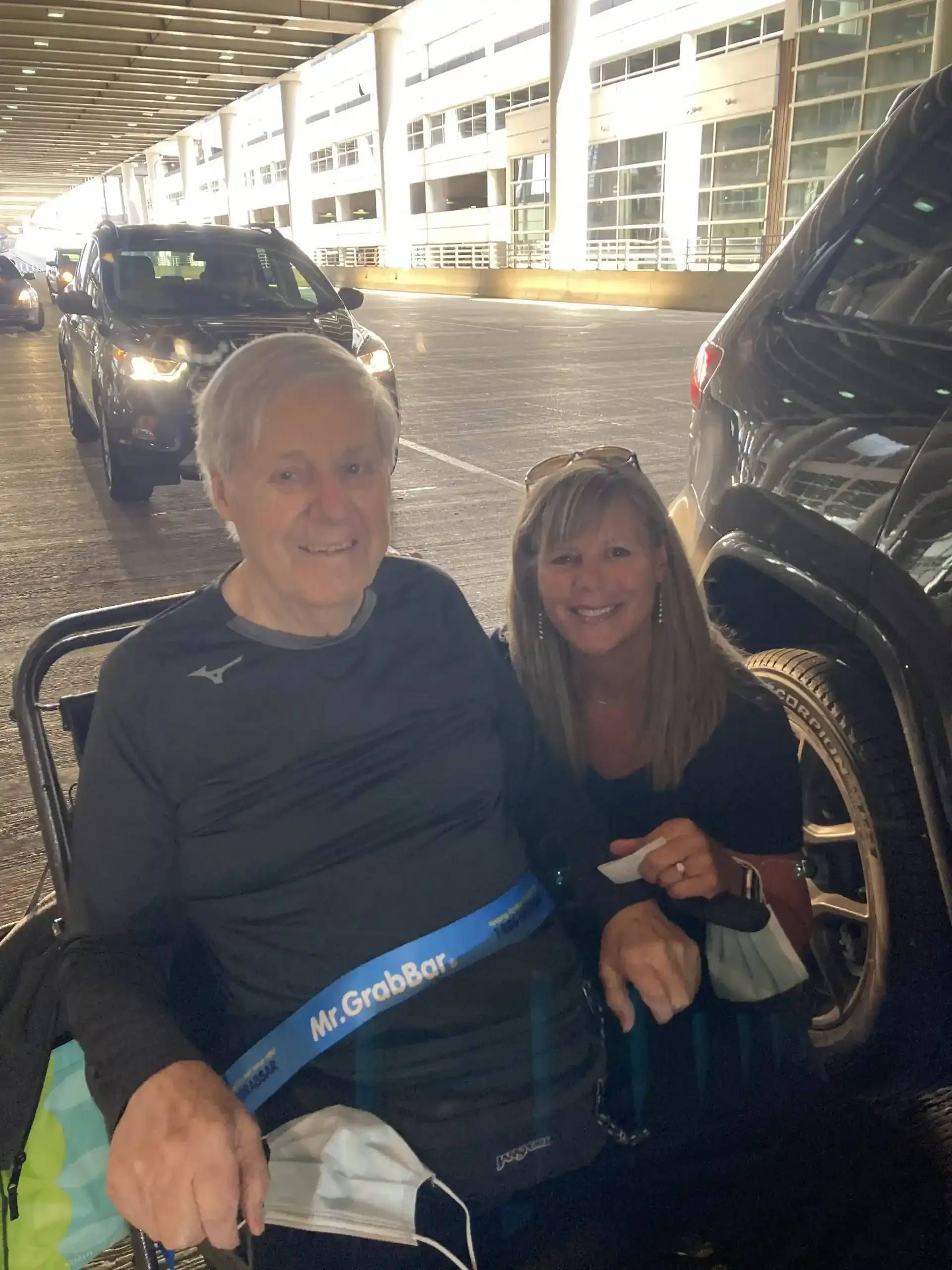 A man in a wheelchair is sitting next to a woman in a parking lot.