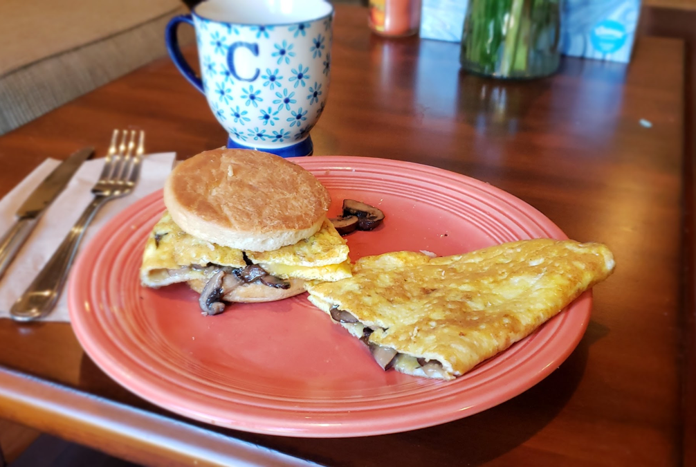 A plate of food with an omelet and a muffin on a table.