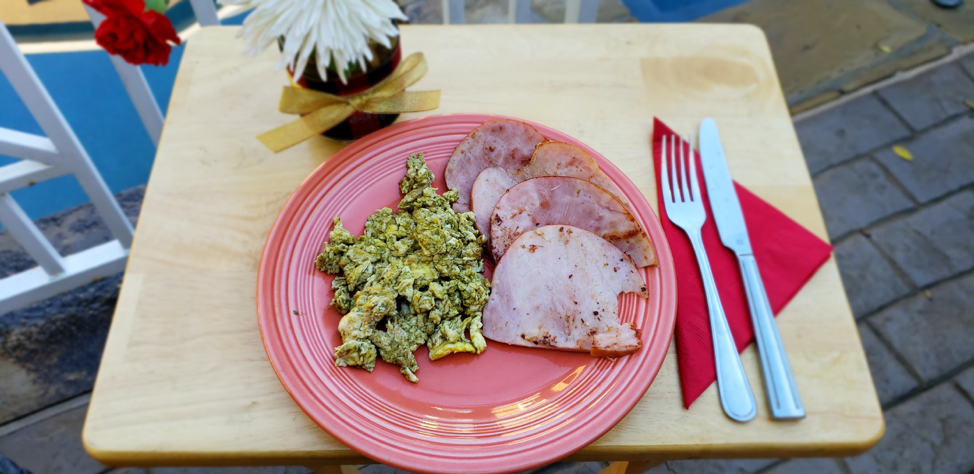 A plate of food with ham and scrambled eggs on a wooden table.