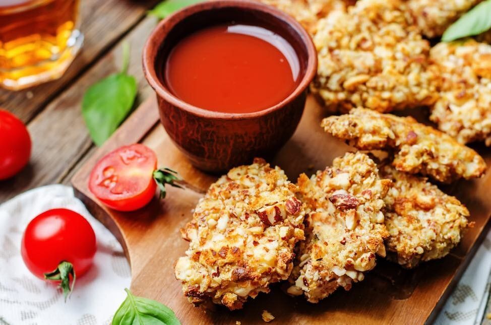 A wooden cutting board topped with chicken nuggets and a bowl of sauce.