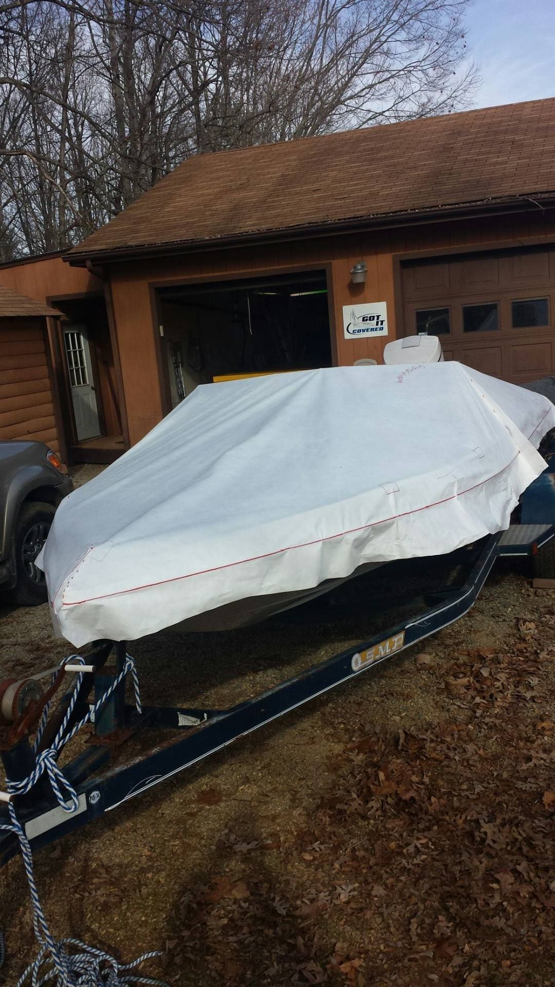 Boat on trailer covered in white tarp in front of a brown building.