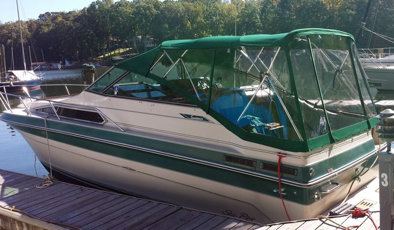 White and green motorboat docked at a marina with a green canvas top.