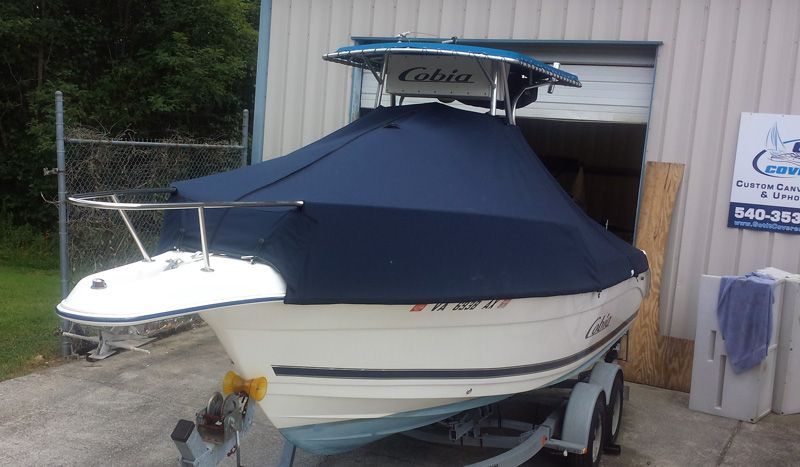 White boat on a trailer, covered with a blue tarp, in front of a building.