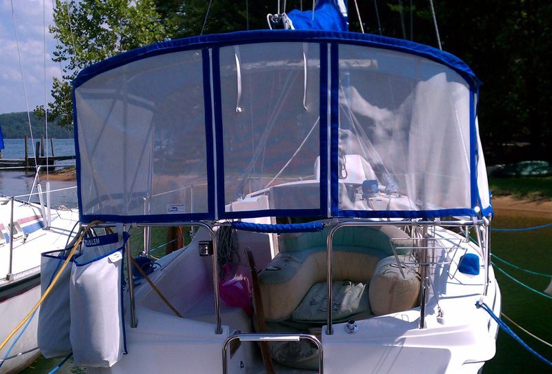 A sailboat stern with a blue-framed enclosure, clear panels, and a cushioned seating area.