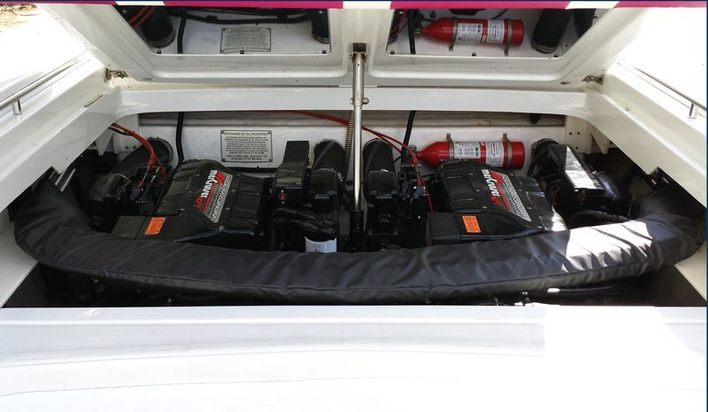 Boat engine compartment with two engines, red fire extinguishers, black engines and black padding.