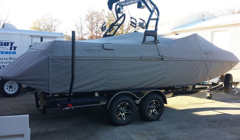 Boat on trailer with gray cover, black tower, and wheels. Outdoors, on a sunny day.