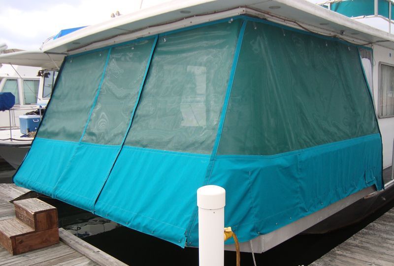 Teal boat enclosure with mesh windows. Attached to a boat at a dock.